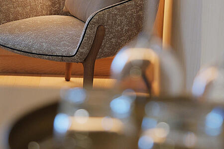 Sitzsessel mit Armlehnen, im Vordergrund unscharf ein Tisch mit Wassergläsern