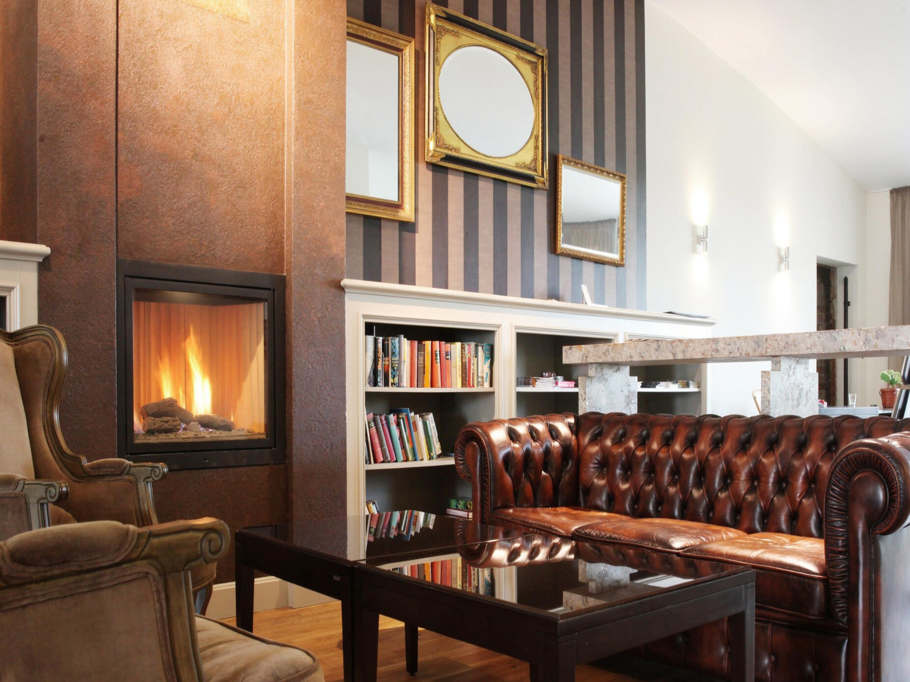 Gemütlicher Hotel-Loungebereich mit Ledersofa, Kamin und Bücherregal.