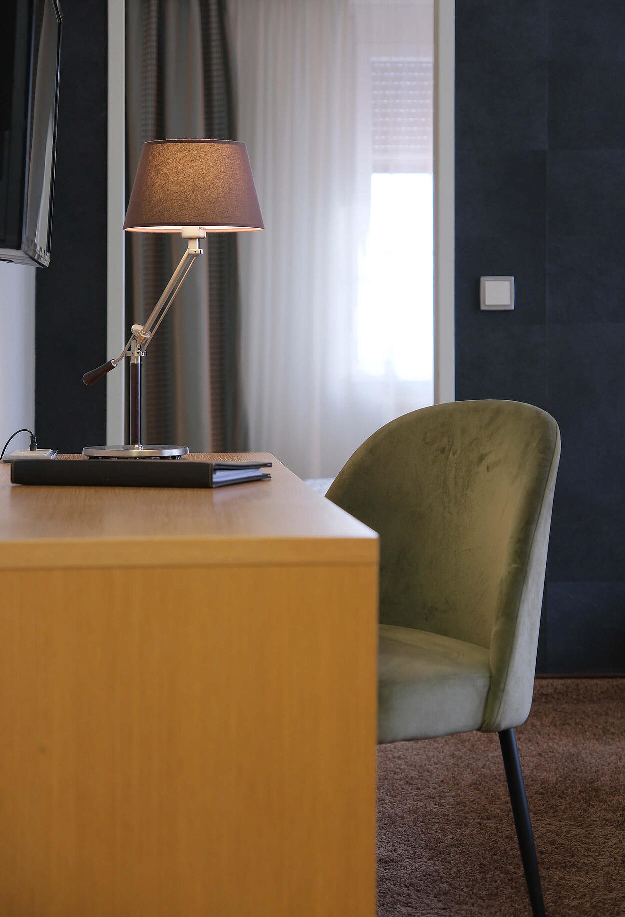 Schreibtisch mit Lampe und grünem Stuhl im ruhigen Zimmerbereich