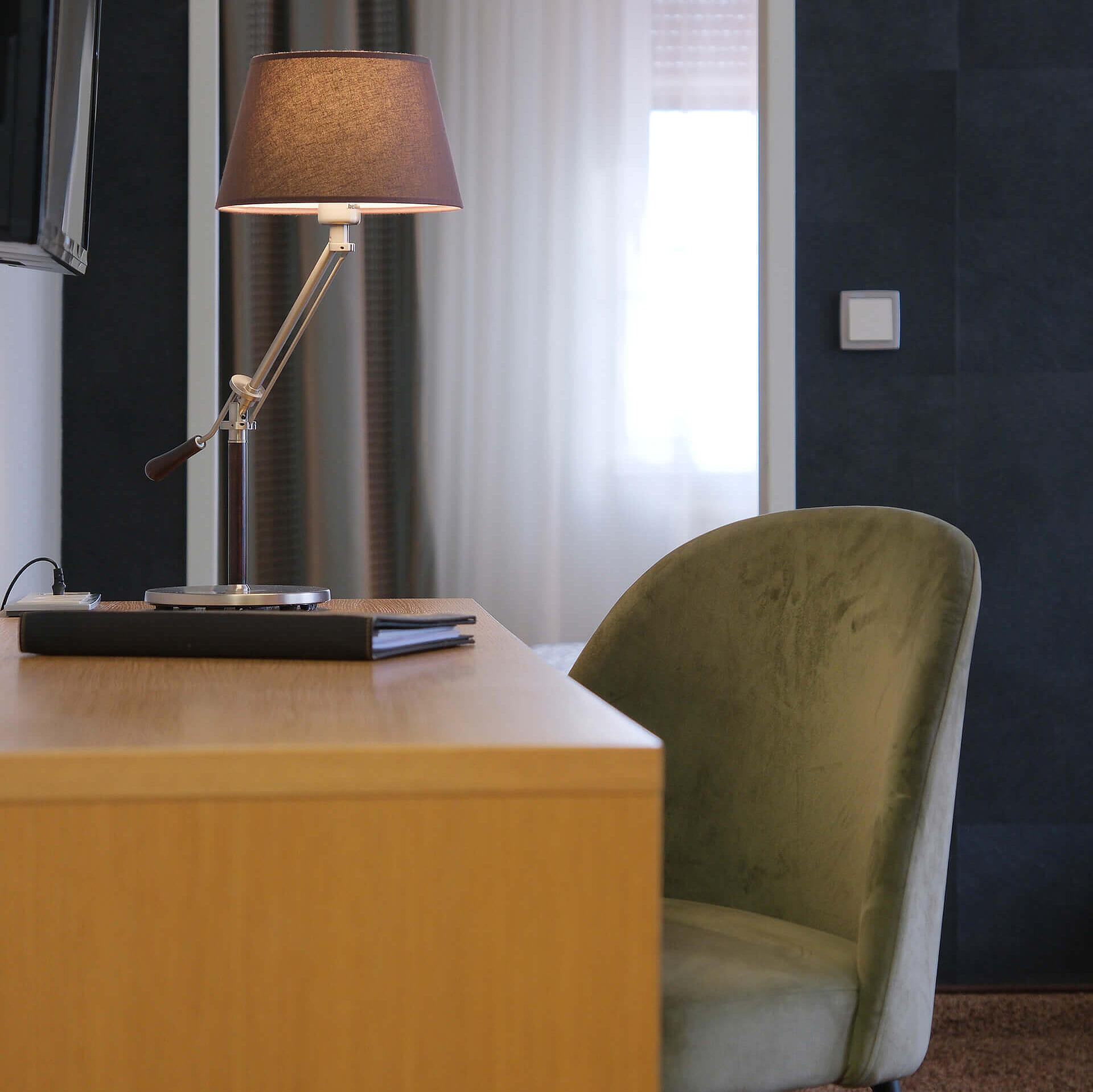 Schreibtisch mit Lampe und grünem Stuhl im ruhigen Zimmerbereich