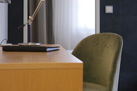 Schreibtisch mit Lampe und grünem Stuhl im ruhigen Zimmerbereich