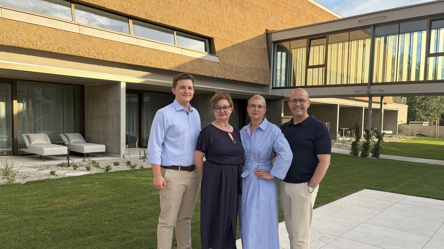 Familie2026quer Vier Personen stehen im Garten vor dem neuen Schilfhaus des Hotel Nationalpark in Illmitz. Im Hintergrund ist die markante, natürlich gestaltete Schilffassade des modernen Hotelzubaus zu sehen.