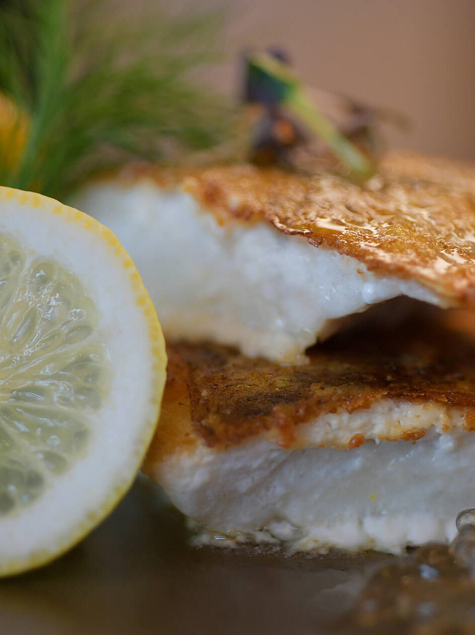 Knusprig gebratener Fisch mit Zitronenscheibe auf dem Teller.