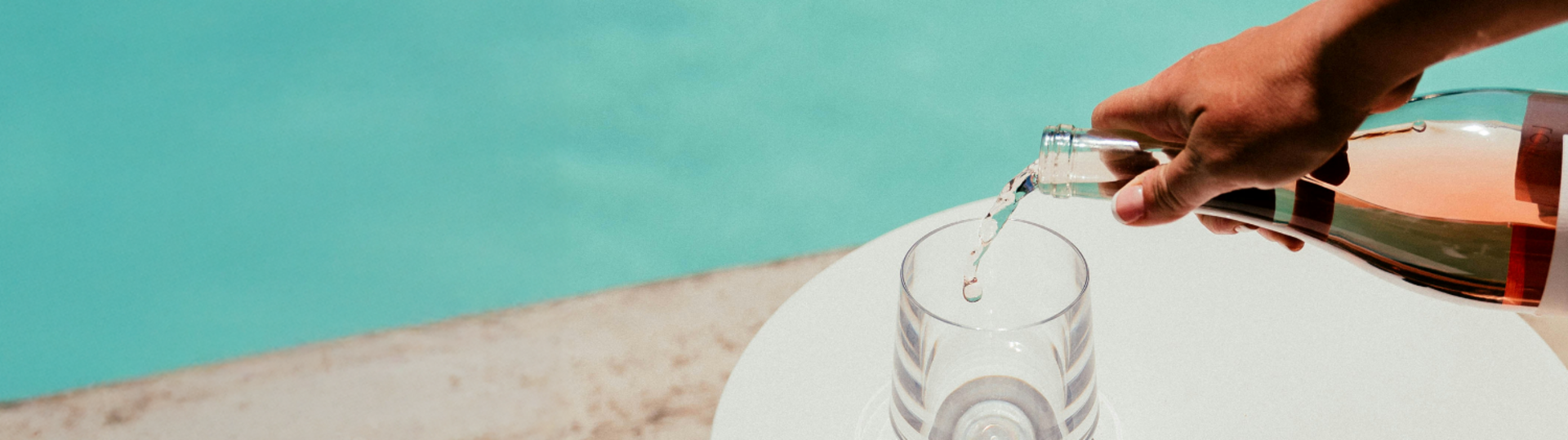 Frizzante wird in ein Glas, das am Poolrand steht, eingefüllt