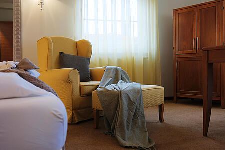 Doppelzimmer mit großem Bett, gelbem Sessel und Fenster mit Vorhängen