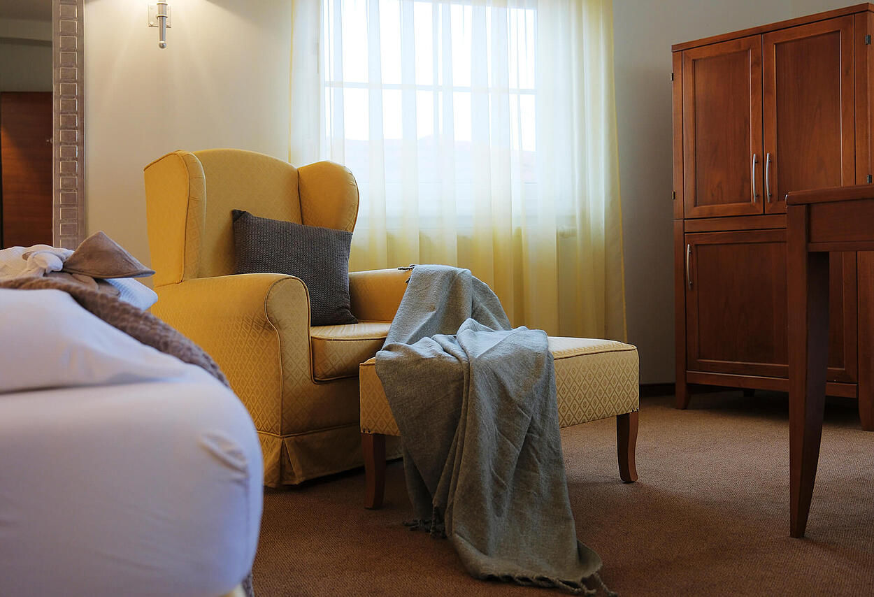 Doppelzimmer mit großem Bett, gelbem Sessel und Fenster mit Vorhängen