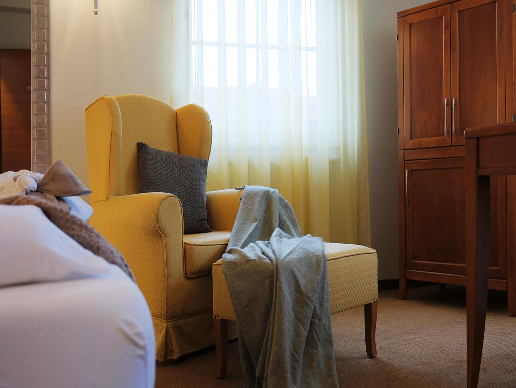 Doppelzimmer mit großem Bett, gelbem Sessel und Fenster mit Vorhängen