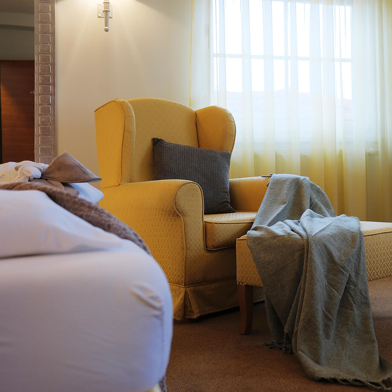 Doppelzimmer mit großem Bett, gelbem Sessel und Fenster mit Vorhängen