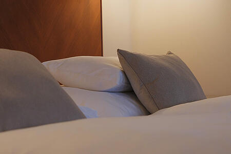 Detailansicht des Bettes mit Kissen und Wandlampe in warmer Beleuchtung