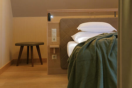 Bett mit Decke und Nachttisch unter dekorativen Hängeleuchten