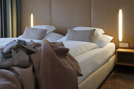 Doppelbett mit Decken und moderner Beleuchtung in warmen Naturtönen