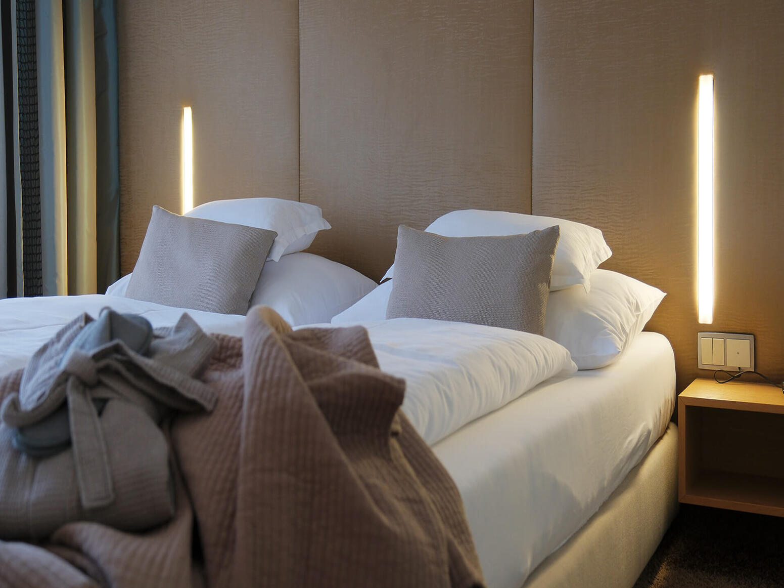 Doppelbett mit Decken und moderner Beleuchtung in warmen Naturtönen