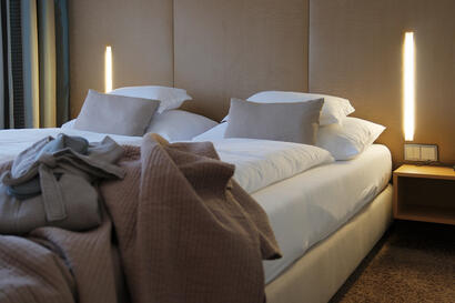 Doppelbett mit Decken und moderner Beleuchtung in warmen Naturtönen