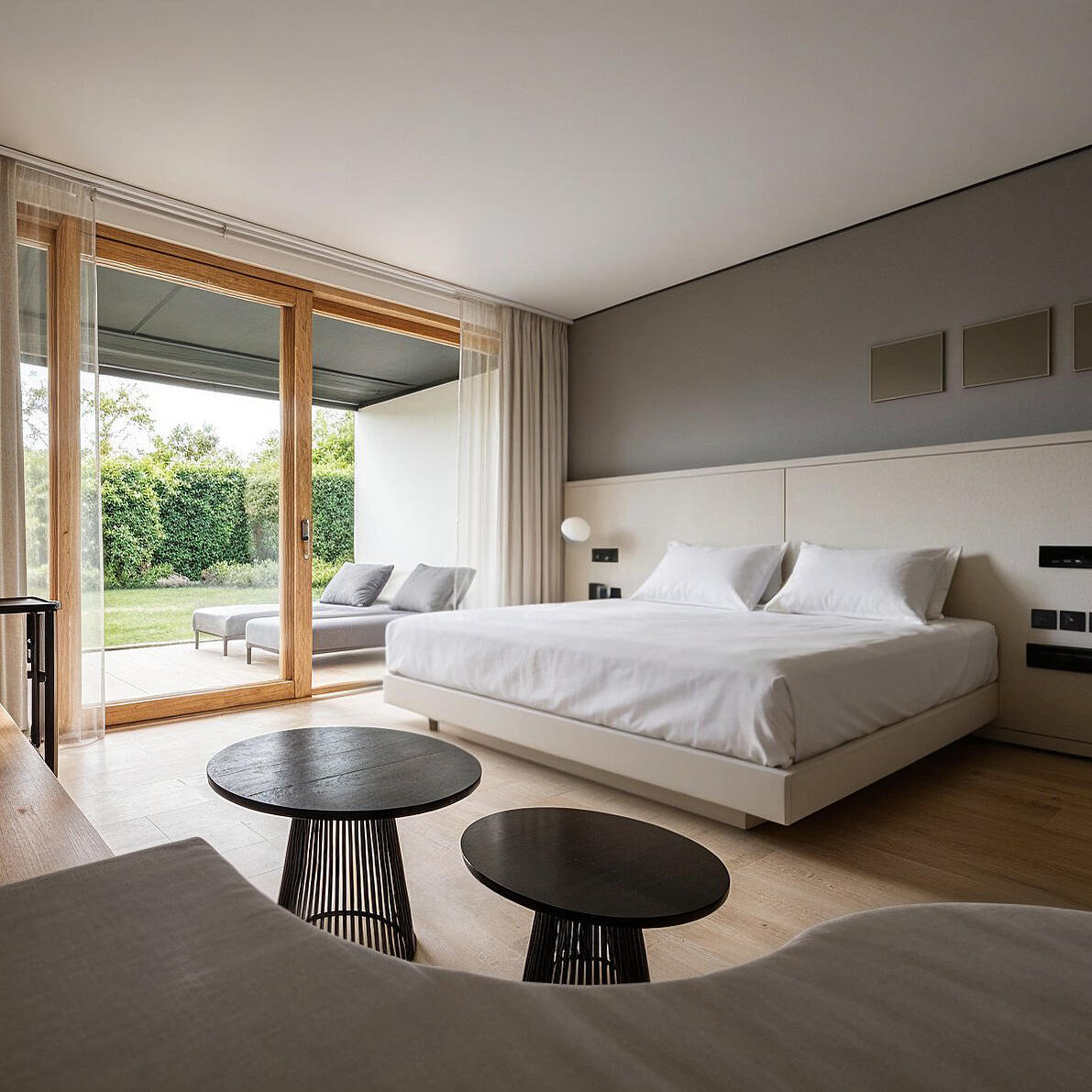 3D-Rendering eines hellen Doppelzimmer mit Holzelementen, großem Bett und Blick zur Gartenterrasse