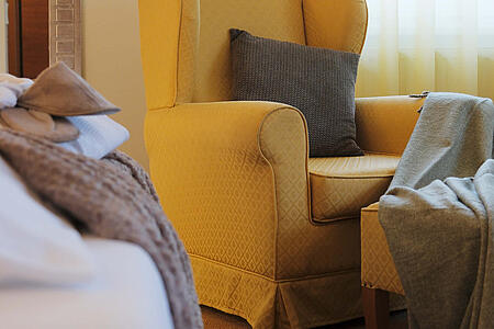 Sitzbereich mit gelbem Ohrensessel neben dem Bett im hellen Zimmer