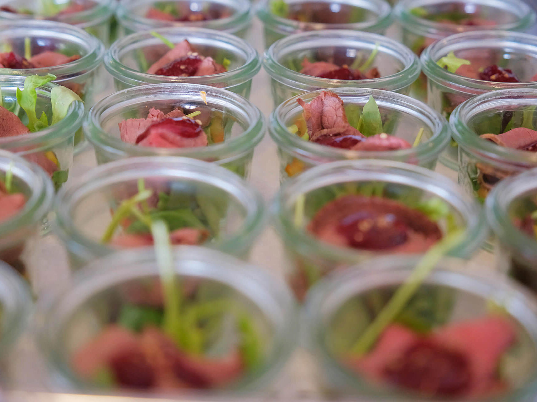 Kleine Vorspeisen in Gläsern mit Kräutern angerichtet.