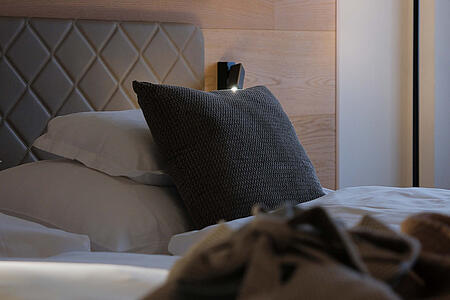 Detailansicht des Bettes mit gepolstertem Kopfteil und dekorativer Leuchte