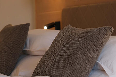 Bett mit Kissen und stimmungsvoller Wandbeleuchtung in warmen Naturtönen