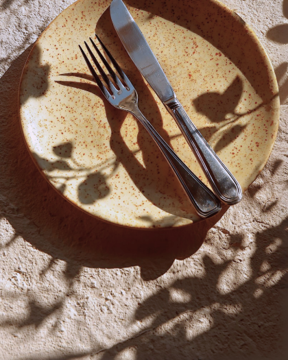 Teller mit Besteck liegt auf hellem Stoff im Sonnenlicht.